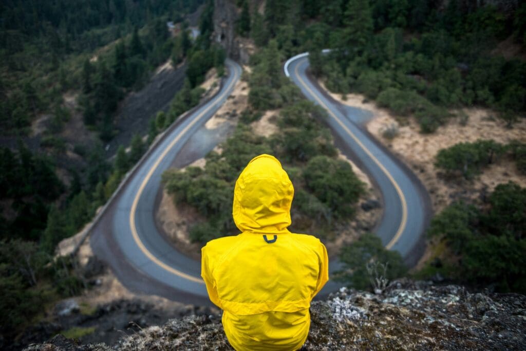 Man in yellow cagoule looking out at hairpin bend in a road.
